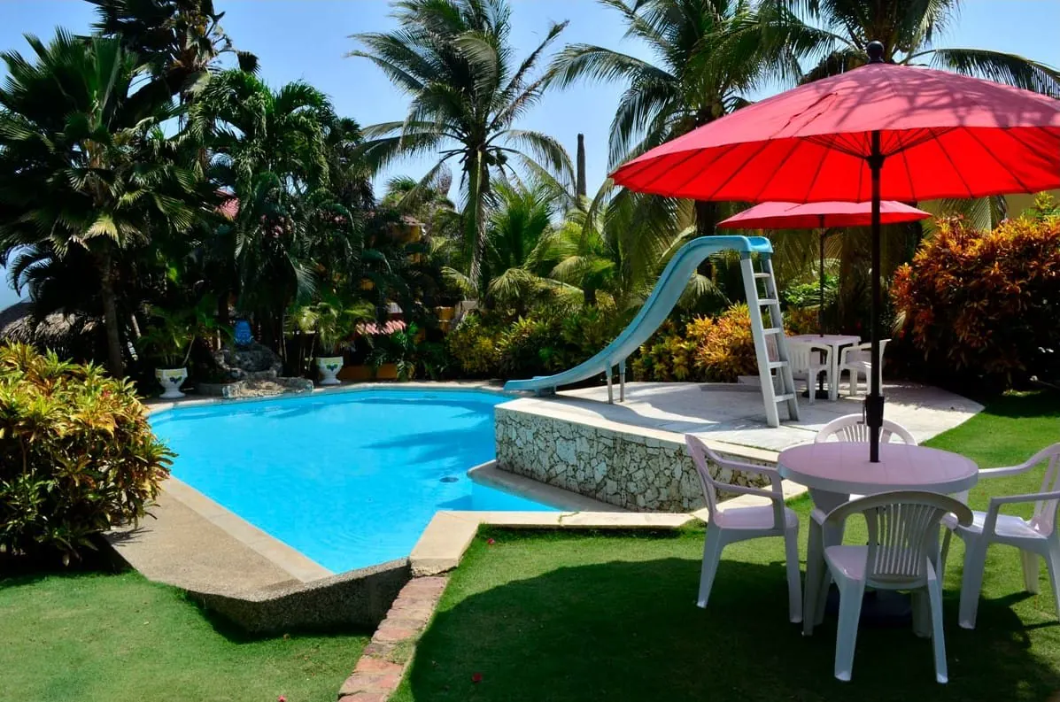 Piscina con tobogán, sombrilla roja y mesa junto al jardín
